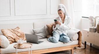woman with towel on head and pyjamas sitting on a sofa and looking at her mobile phone